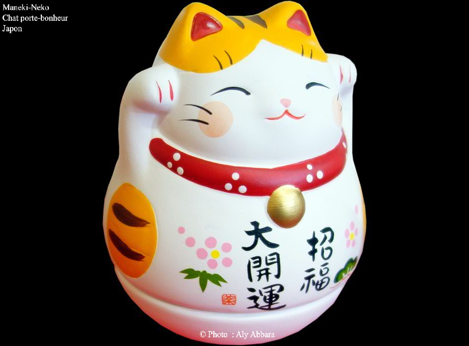 Maneki-Neko à forme simple, blanc avec des taches noires et rousses et enfin une écharpe rouge et une clochette dorée