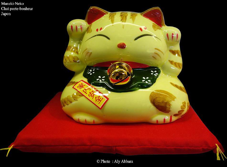 Maneki-Neko jaune levant ses deux pattes de devant  (version mixte féminine et masculine) portant un collier (écharpe) rouge à petite clochette